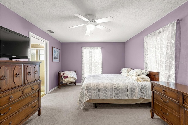 bedroom with a textured ceiling, ceiling fan, light carpet, and connected bathroom