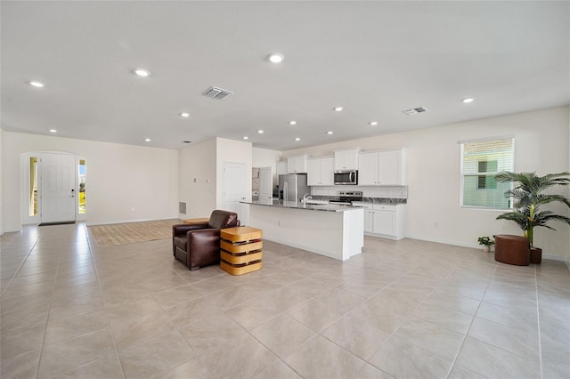 kitchen featuring light stone countertops, appliances with stainless steel finishes, a breakfast bar, a kitchen island with sink, and white cabinets