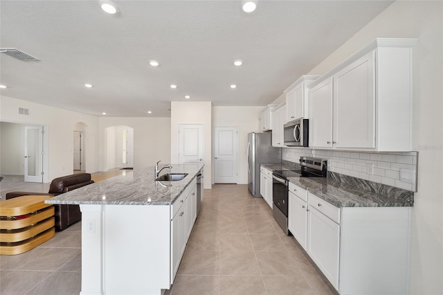 kitchen featuring stainless steel appliances, white cabinetry, dark stone countertops, and an island with sink