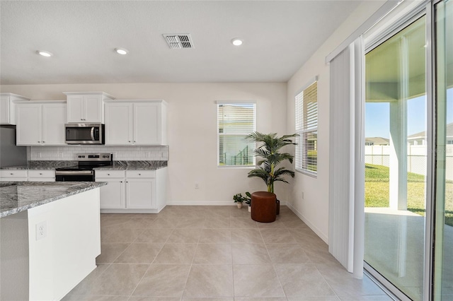 kitchen featuring light tile patterned floors, light stone countertops, appliances with stainless steel finishes, tasteful backsplash, and white cabinetry