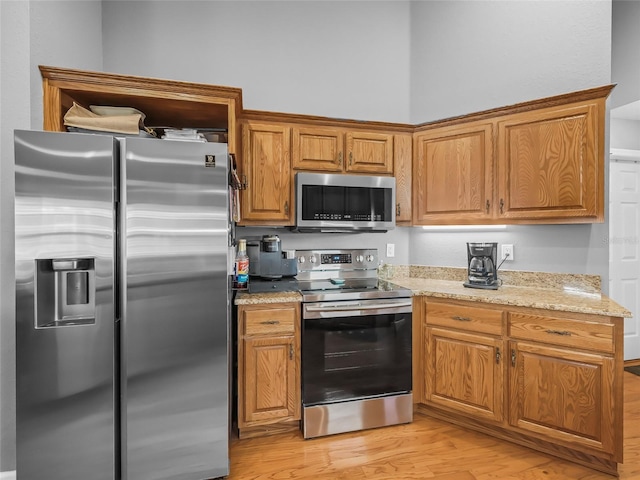 kitchen with appliances with stainless steel finishes, light wood-type flooring, and light stone counters