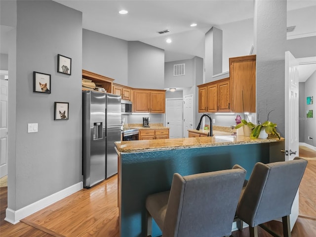 kitchen with kitchen peninsula, a kitchen breakfast bar, a towering ceiling, light wood-type flooring, and stainless steel appliances