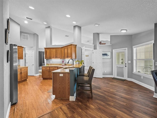 kitchen with light stone countertops, sink, dark wood-type flooring, kitchen peninsula, and a kitchen bar