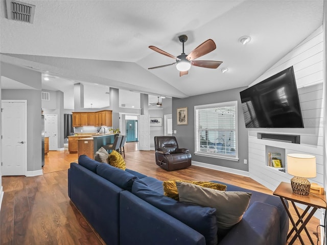 living room featuring a textured ceiling, light hardwood / wood-style floors, lofted ceiling, and sink