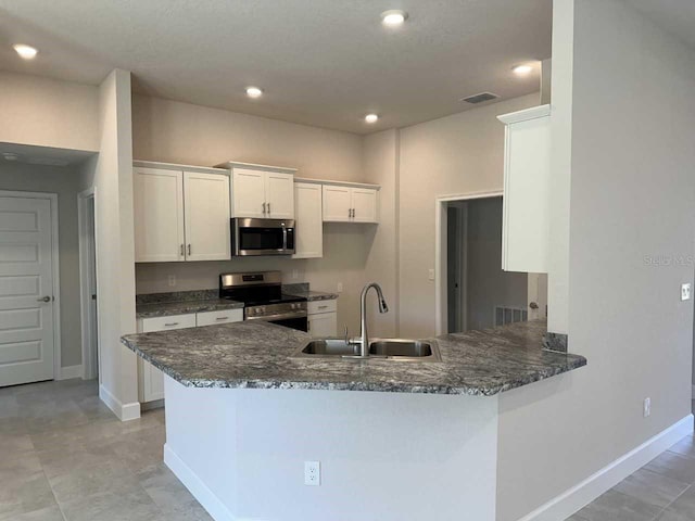 kitchen with white cabinets, sink, dark stone countertops, kitchen peninsula, and stainless steel appliances