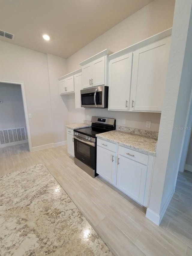 kitchen featuring light stone countertops, white cabinetry, stainless steel appliances, and light hardwood / wood-style floors