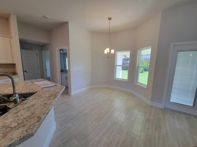 kitchen featuring white cabinetry, sink, light stone counters, decorative light fixtures, and light wood-type flooring