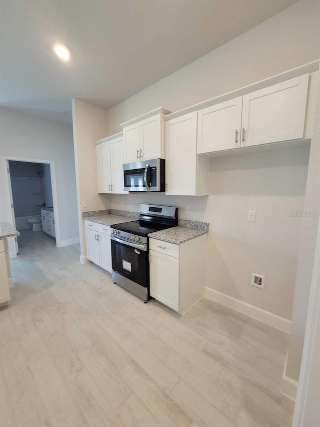 8309 SW 58th Ave, Ocala, FL 34476 - kitchen featuring appliances with stainless steel finishes, white cabinets, light stone countertops, and light wood-style flooring