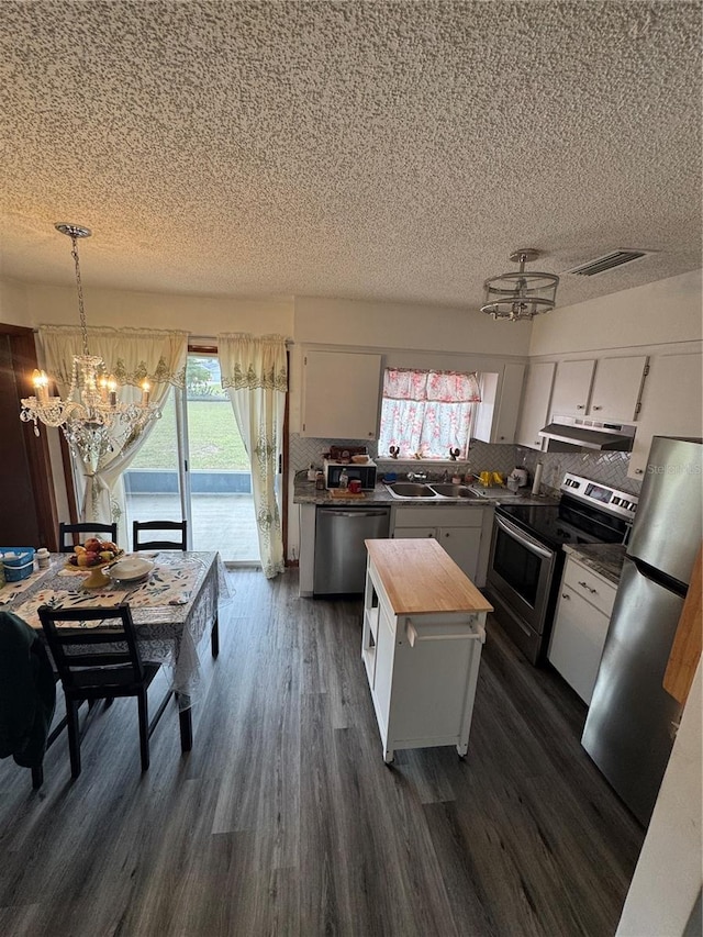 kitchen featuring butcher block counters, decorative light fixtures, a kitchen island, stainless steel appliances, and white cabinets