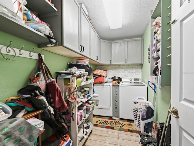 laundry area with cabinets, a textured ceiling, washing machine and dryer, and light hardwood / wood-style flooring