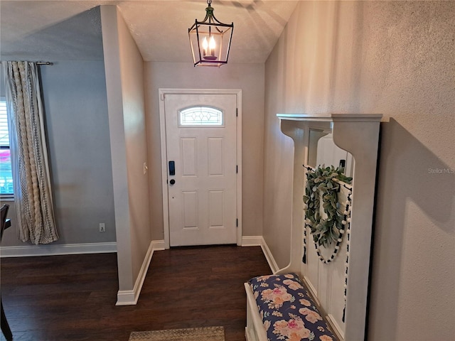 foyer entrance featuring a textured ceiling, dark wood-type flooring, a wealth of natural light, and an inviting chandelier