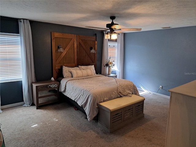 bedroom with multiple windows, a textured ceiling, light colored carpet, and ceiling fan