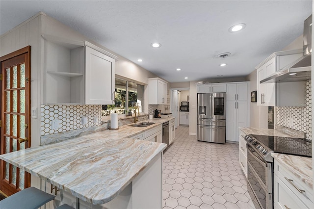 kitchen with a breakfast bar, white cabinets, sink, wall chimney exhaust hood, and appliances with stainless steel finishes