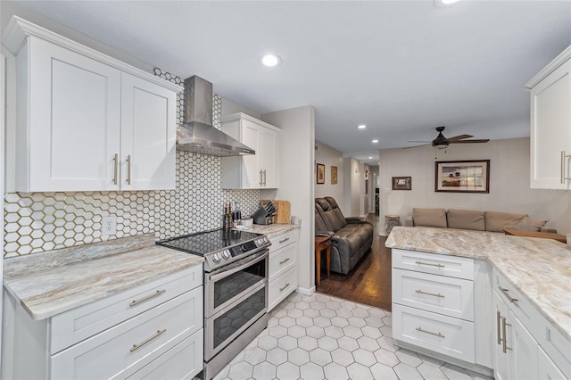 kitchen featuring ceiling fan, wall chimney exhaust hood, light hardwood / wood-style flooring, double oven range, and white cabinets