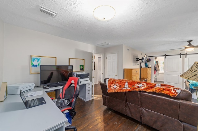 home office featuring a barn door, ceiling fan, dark wood-type flooring, and a textured ceiling