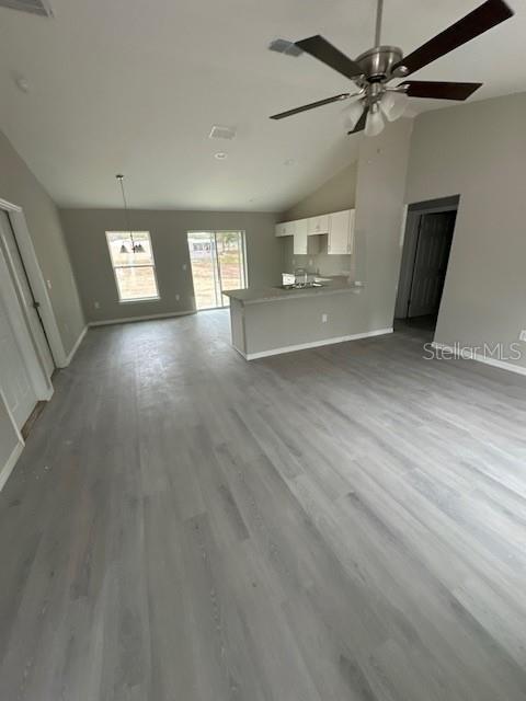 unfurnished living room featuring ceiling fan, baseboards, vaulted ceiling, and wood finished floors