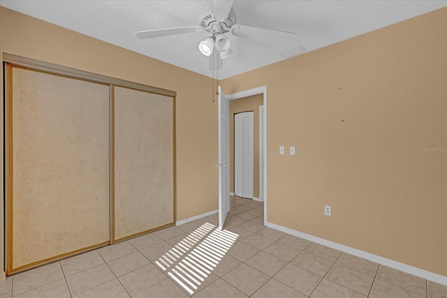 unfurnished bedroom featuring light tile patterned floors, a textured ceiling, a closet, and ceiling fan