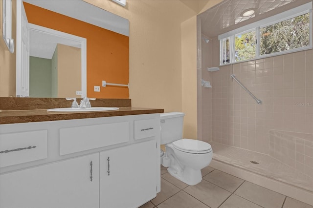 bathroom with tile patterned flooring, toilet, a tile shower, and vanity