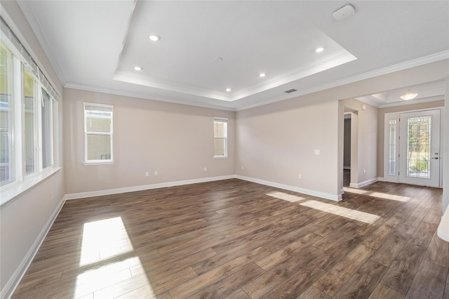 empty room with a raised ceiling, crown molding, and dark wood-type flooring