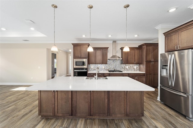 kitchen featuring wall chimney exhaust hood, stainless steel appliances, sink, hanging light fixtures, and a large island