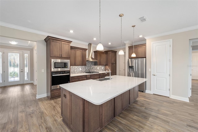 kitchen with hardwood / wood-style floors, a center island with sink, wall chimney range hood, ornamental molding, and stainless steel appliances