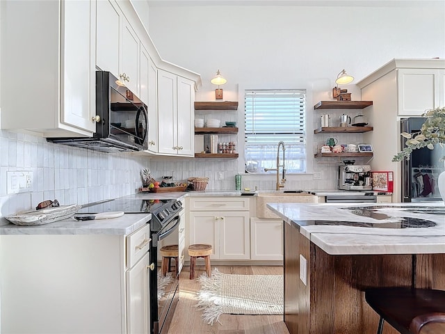 kitchen featuring white cabinetry, light hardwood / wood-style flooring, backsplash, a breakfast bar, and black appliances