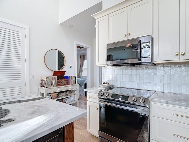 kitchen featuring tasteful backsplash, light stone counters, light hardwood / wood-style floors, and appliances with stainless steel finishes