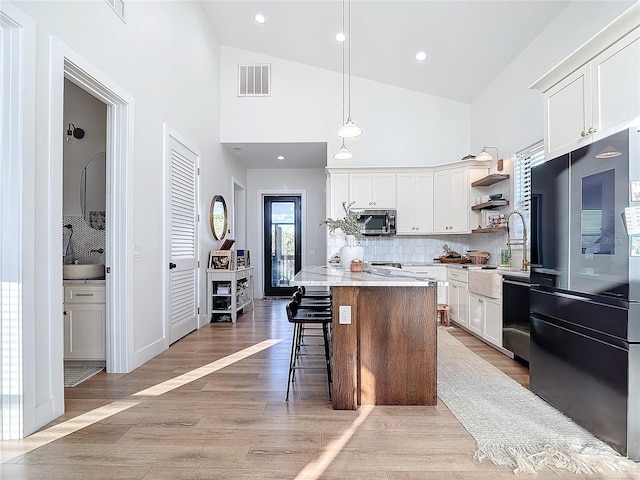 kitchen with black appliances, a kitchen island, white cabinetry, and light hardwood / wood-style floors