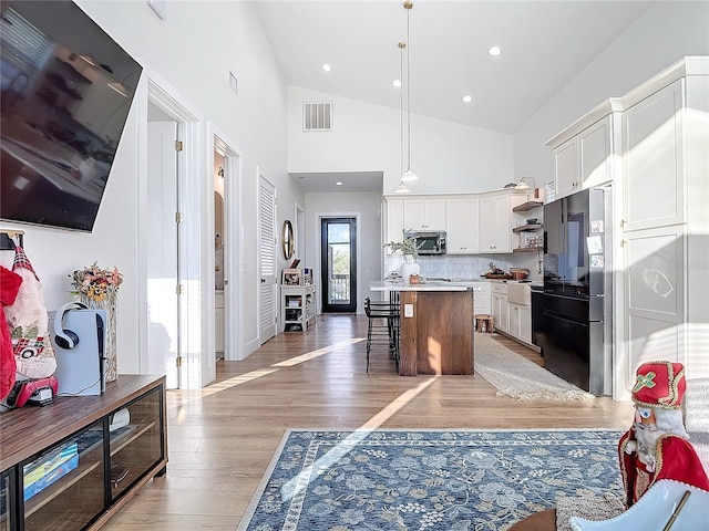 kitchen featuring black refrigerator, a kitchen breakfast bar, a center island, white cabinetry, and hanging light fixtures