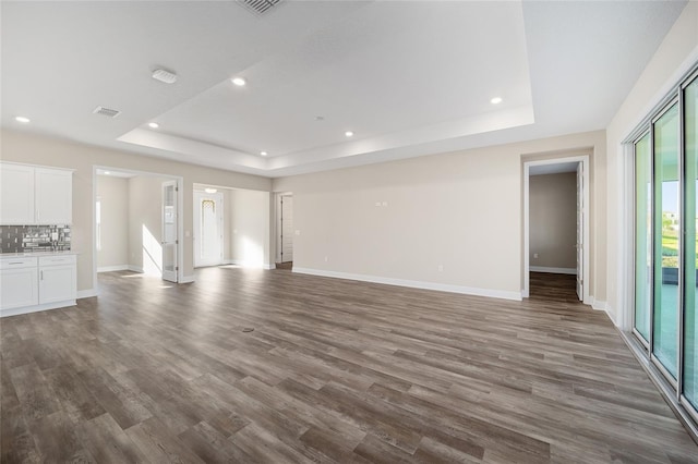 unfurnished living room featuring a tray ceiling and dark hardwood / wood-style flooring