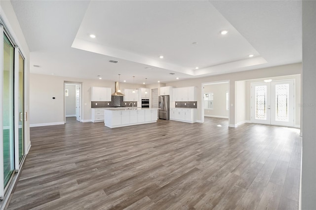 unfurnished living room featuring a raised ceiling, wood-type flooring, sink, and french doors