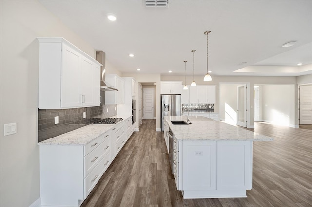 kitchen with a spacious island, white cabinetry, hanging light fixtures, and wall chimney range hood