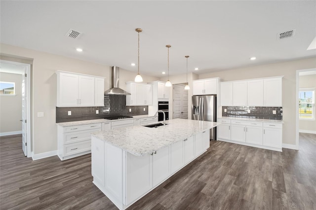 kitchen featuring white cabinets, a center island with sink, wall chimney exhaust hood, and sink