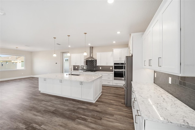 kitchen with dark hardwood / wood-style flooring, wall chimney exhaust hood, decorative light fixtures, white cabinetry, and an island with sink