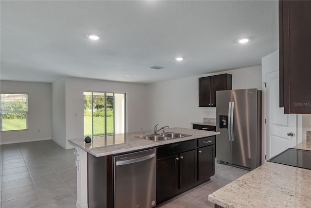 kitchen with a kitchen island with sink, sink, light tile patterned flooring, light stone counters, and stainless steel appliances