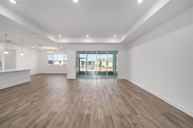 unfurnished living room with dark wood-type flooring, a tray ceiling, and an inviting chandelier