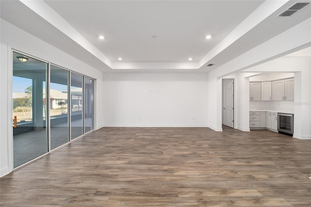 unfurnished living room with wood-type flooring, a tray ceiling, and wine cooler