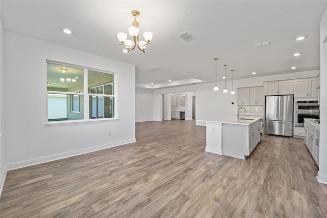 kitchen with stainless steel appliances, sink, a chandelier, hanging light fixtures, and an island with sink