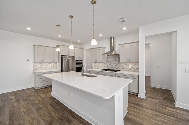 kitchen featuring sink, wall chimney exhaust hood, dark hardwood / wood-style floors, an island with sink, and appliances with stainless steel finishes