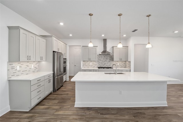 kitchen with wall chimney exhaust hood, sink, dark hardwood / wood-style floors, hanging light fixtures, and an island with sink