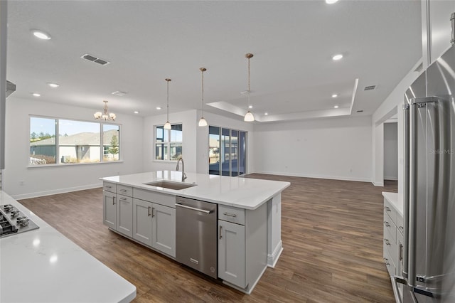 kitchen with dark hardwood / wood-style flooring, stainless steel appliances, sink, a center island with sink, and hanging light fixtures