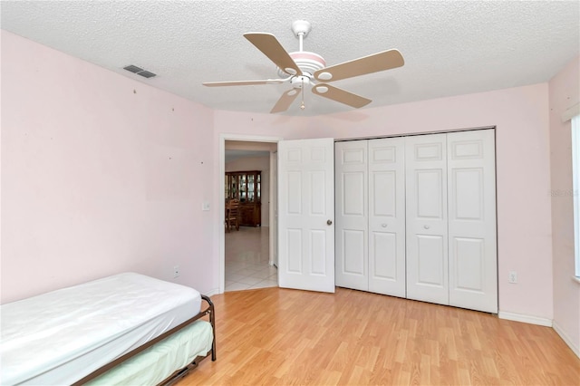 bedroom featuring ceiling fan, light wood-type flooring, a textured ceiling, and a closet