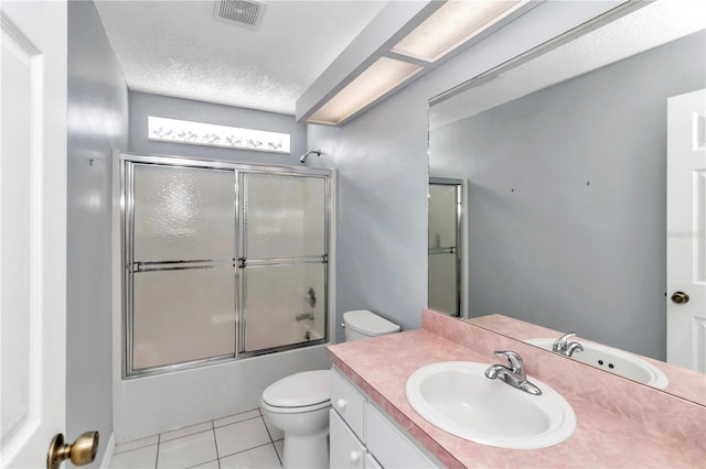 full bathroom featuring tile patterned floors, bath / shower combo with glass door, a textured ceiling, toilet, and vanity