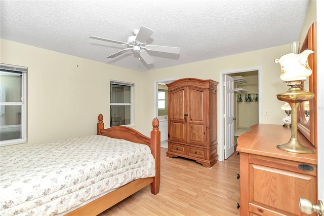 bedroom with ceiling fan, a walk in closet, light wood-type flooring, and a textured ceiling