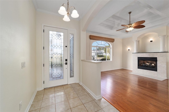 foyer entrance with a tile fireplace, crown molding, ceiling fan with notable chandelier, and light wood-type flooring