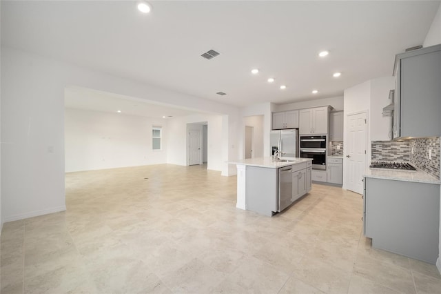 kitchen featuring a center island with sink, decorative backsplash, gray cabinets, and stainless steel appliances