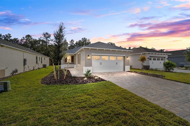 view of front of property with central AC, a garage, and a lawn