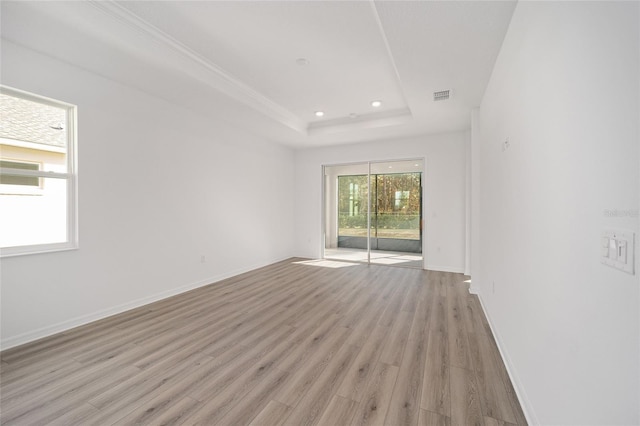 empty room with light hardwood / wood-style floors, a tray ceiling, and a healthy amount of sunlight