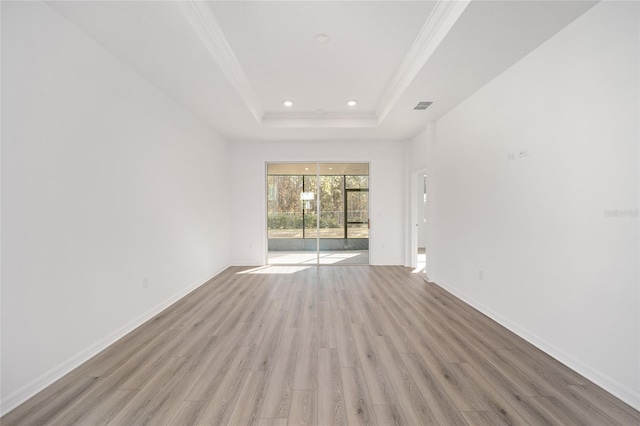 empty room with a raised ceiling, ornamental molding, and light wood-type flooring