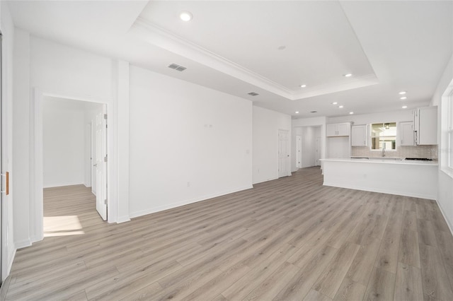 unfurnished living room with a tray ceiling, crown molding, and light hardwood / wood-style floors